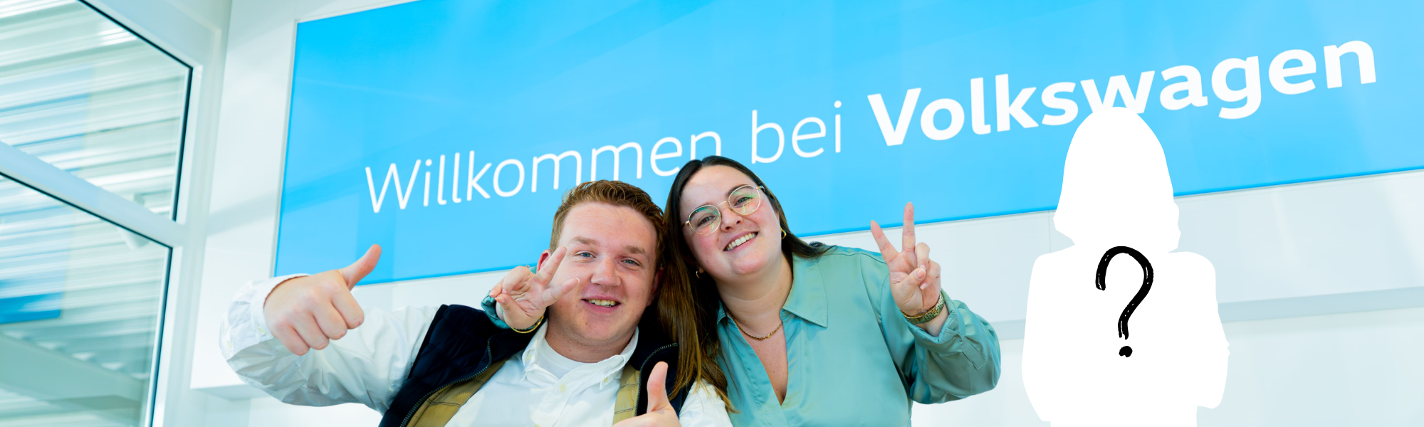 Zwei lächelnde Kollegen vor einem Schild "Willkommen bei Volkswagen".